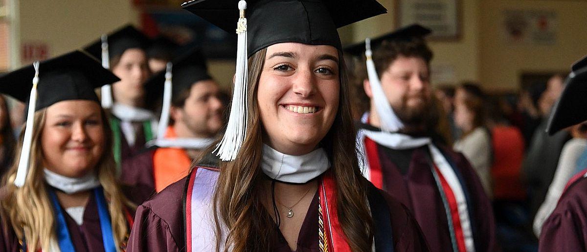 Graduate smiling at the camera as a group of graduates walk into the 2024 Commencement ceremony.